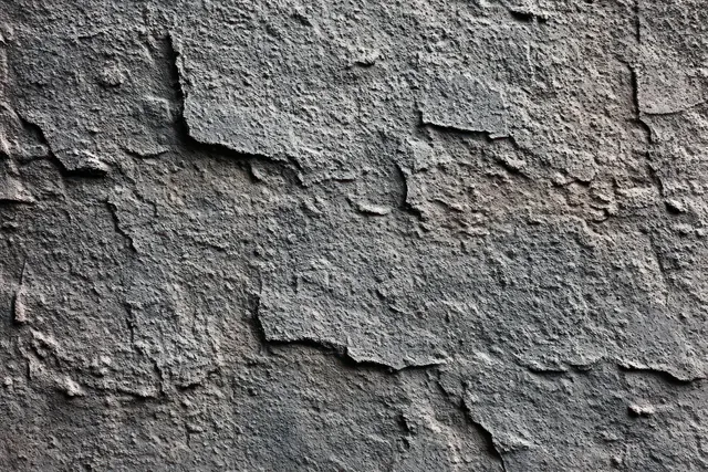 Close-up of peeling, cracked paint on a rough gray concrete wall exposing underlying layers.
