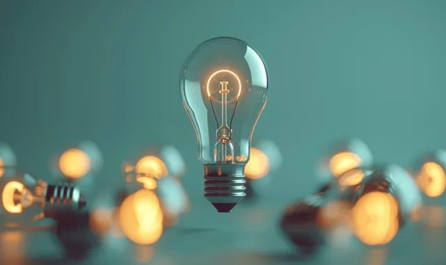 Glowing light bulb stands out among darker bulbs on a pastel green background with soft bokeh lights.