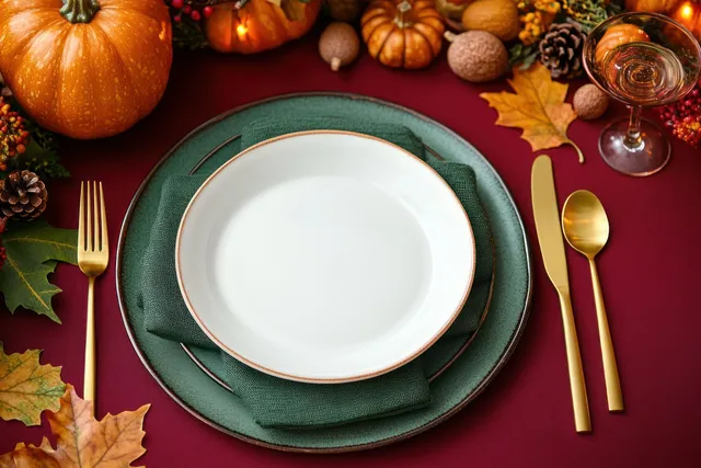 Top view of a Thanksgiving table setting with white plates, gold cutlery, pumpkins, and autumn leaves.