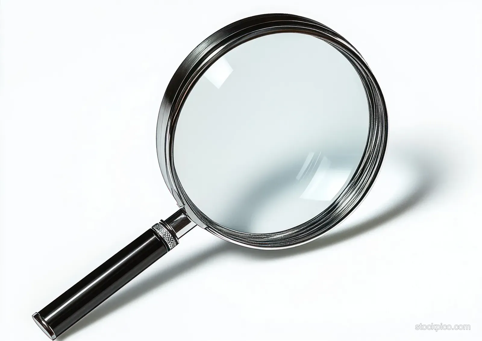 A handheld magnifying glass lies on a white surface, showing its circular lens rim and sharp shadow.