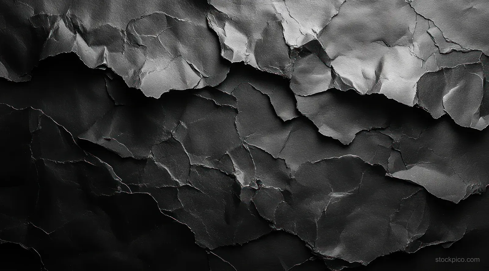 Crumpled black paper poster with blank surface against a textured gray wall with dramatic creases.