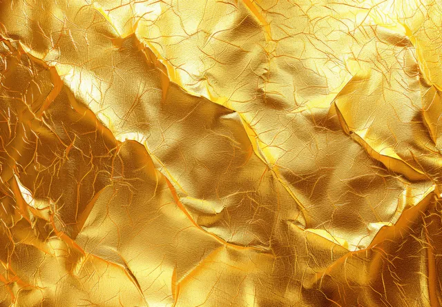 Close-up of crinkled gold foil paper with bright reflective highlights and textured folds.