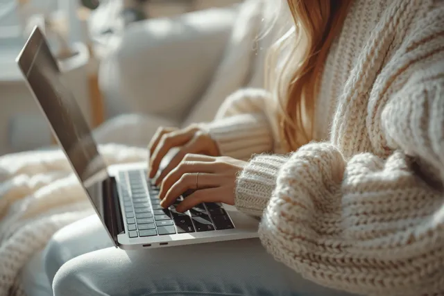 Woman’s hands typing on a laptop keyboard on a clean white desk in a softly lit office setting.