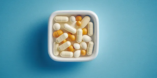 Assorted white and orange pills and capsules are visible inside a small square container on a textured blue background.