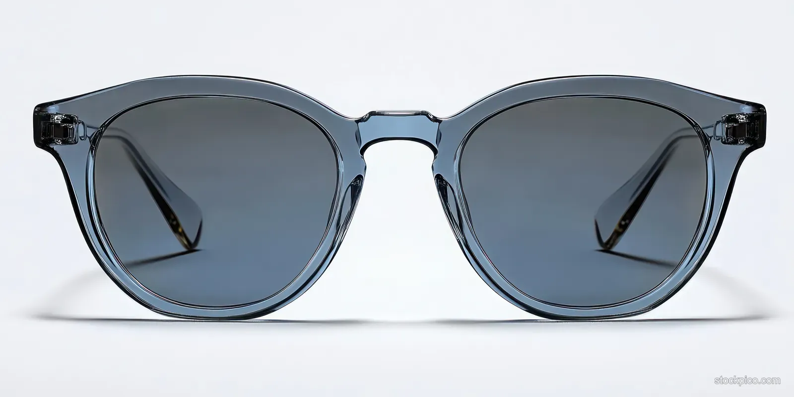 Smoky blue transparent sunglasses with dark lenses lying on a white surface under bright light.