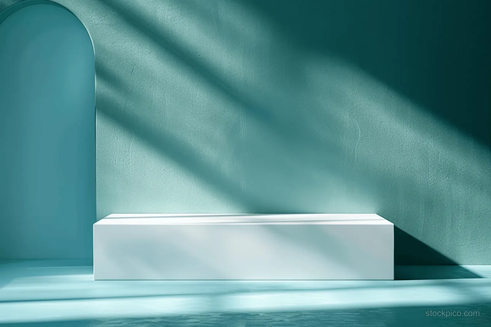 White rectangular bench sits against teal wall in a minimalist interior with dramatic sunlight shadows.
