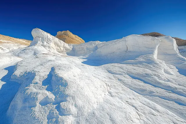 White sandstone desert dunes and rock arches curve across a landscape under a clear deep blue sky.
