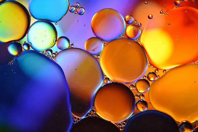 Close-up oil droplets floating in water forming vibrant blue-orange-purple abstract liquid circles