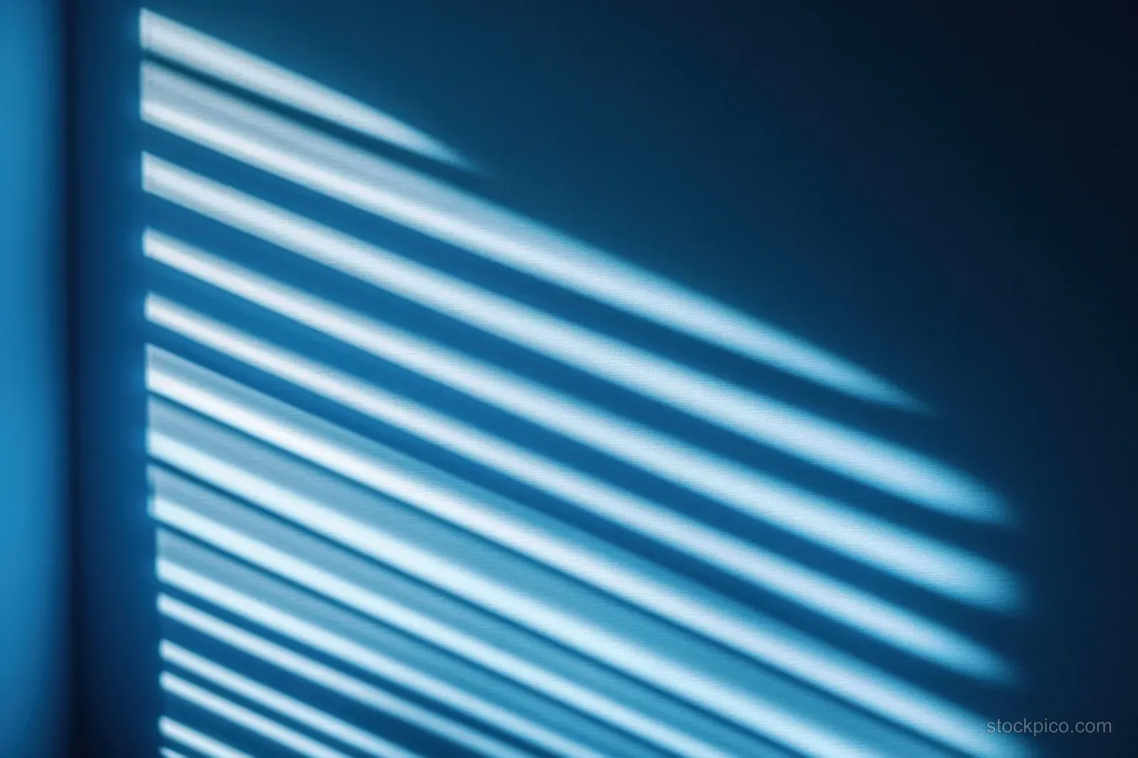 Soft sunlight through window blinds casts parallel striped shadows on a smooth blue wall.