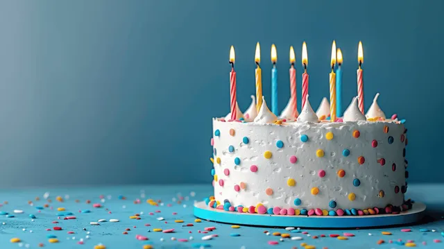 Birthday cake with white frosting, rainbow sprinkles, and several lit candles on a blue background.
