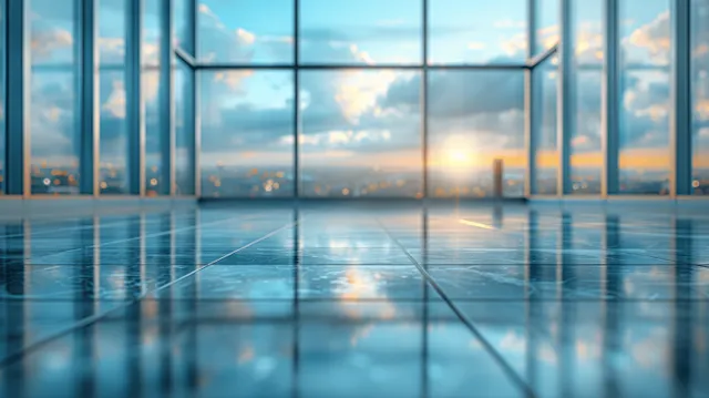 Empty modern office interior with panoramic glass windows and a glass conference table reflecting sunset light.
