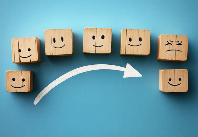 Wooden blocks with sad and happy faces are arranged in sequence, with a white arrow pointing toward happiness on a blue background.