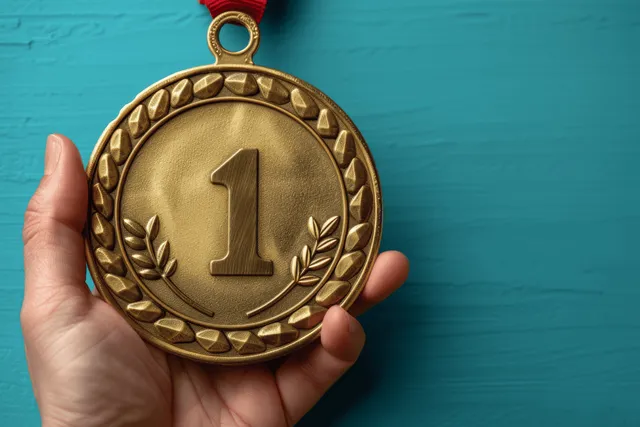 A hand holds a gold first-place medal with a number one and laurel design on a blue background.
