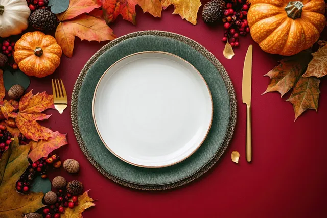 Top view of a Thanksgiving table setting with a white plate, gold cutlery, pumpkins, and autumn leaves.