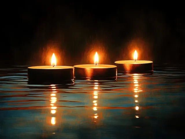 Three tealight candles floating on calm water, glowing reflections in a dark nighttime scene
