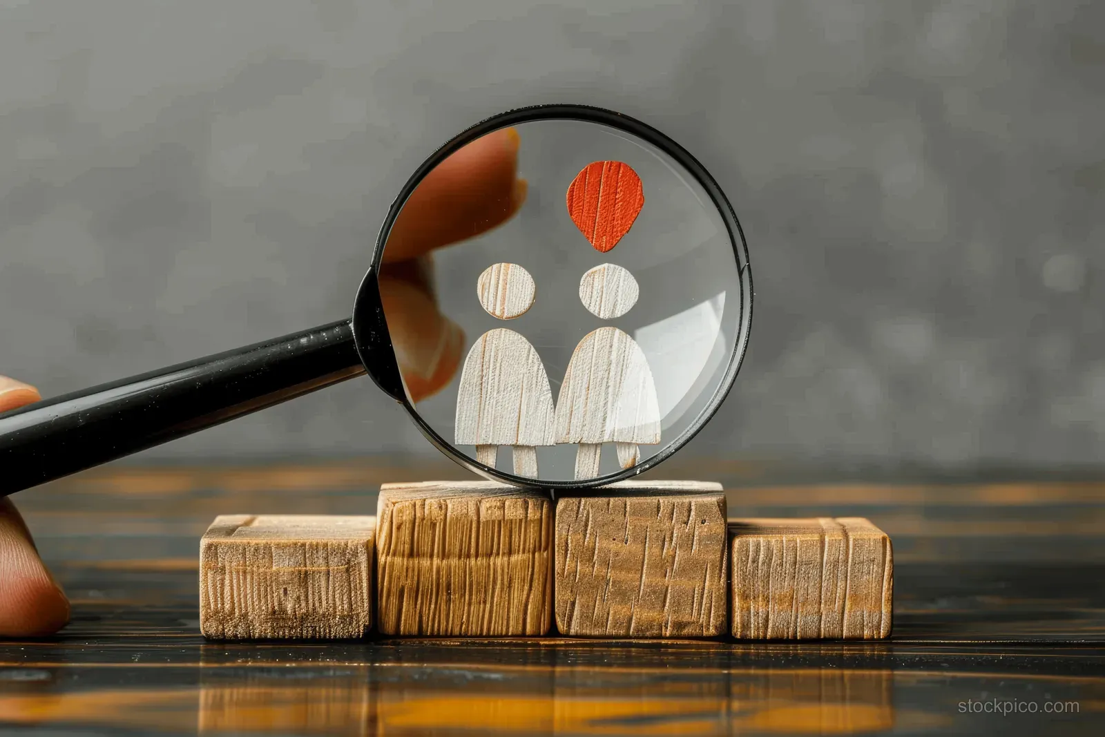 A magnifying glass highlights person icons on stacked wood blocks with a dark gray backdrop.