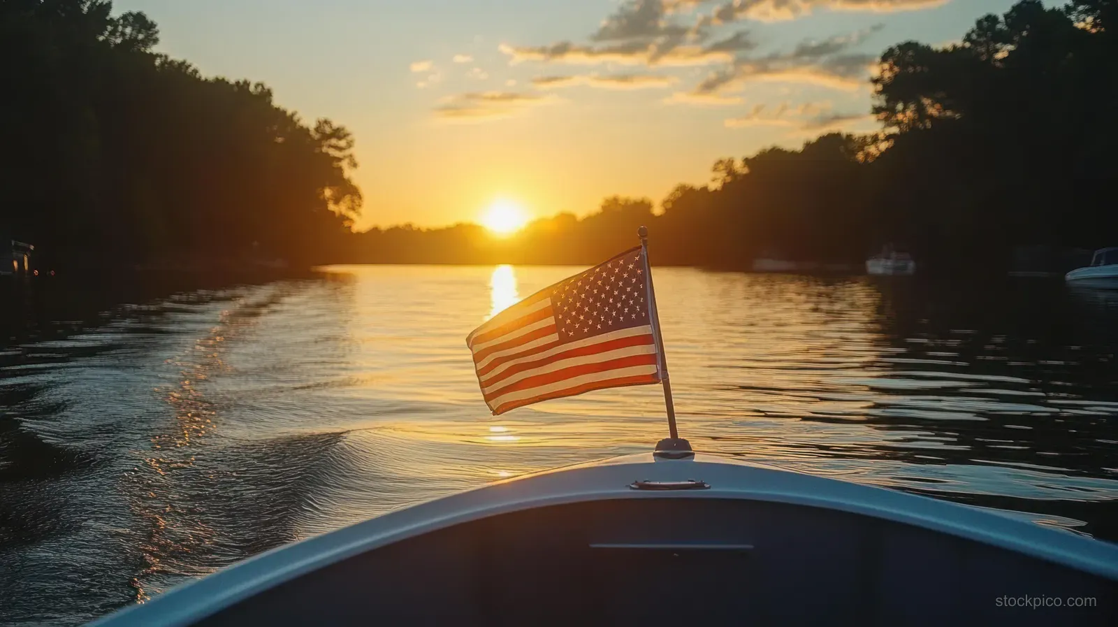 American flag waves at the boat stern as the vessel cruises across a calm lake during sunset with silhouetted trees.