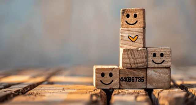 Wooden blocks with smiley faces and check marks stacked on a staircase pattern to show successful progress.
