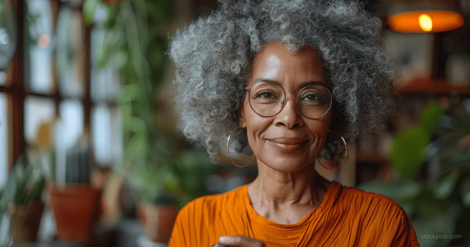 Smiling African American senior woman with curly gray hair holds a smartphone in a warmly lit home living room.