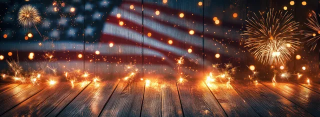 Sparklers and fireworks illuminate an American flag resting on rustic wooden planks with warm spark trails.