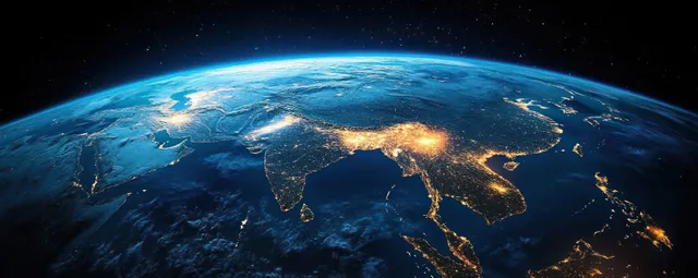 View of Earth from space at dusk with India and Himalayan terrain illuminated by city lights.