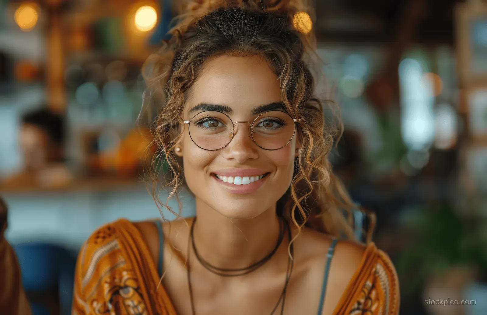 Smiling businesswoman in glasses sits at a table with a laptop surrounded by colleagues during an office meeting.