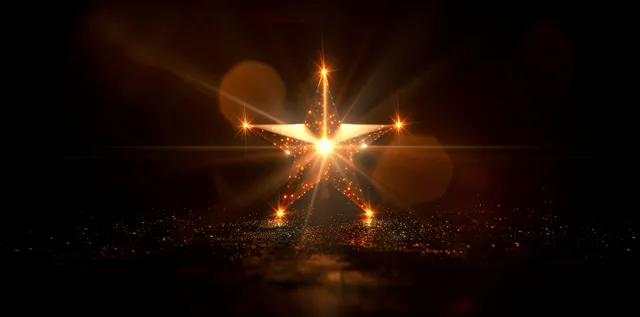 Golden starburst lens flare with warm sun rays radiating outward on a black background.