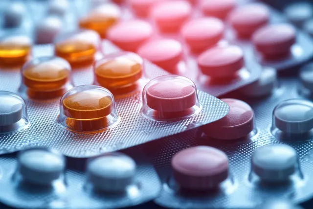 Orange and pink round tablets rest inside plastic blister packs under bright soft lighting.