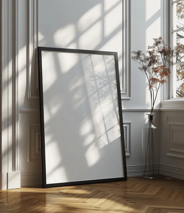Black picture frame mockup leaning by a window with sunlight shadows on a parquet floor.