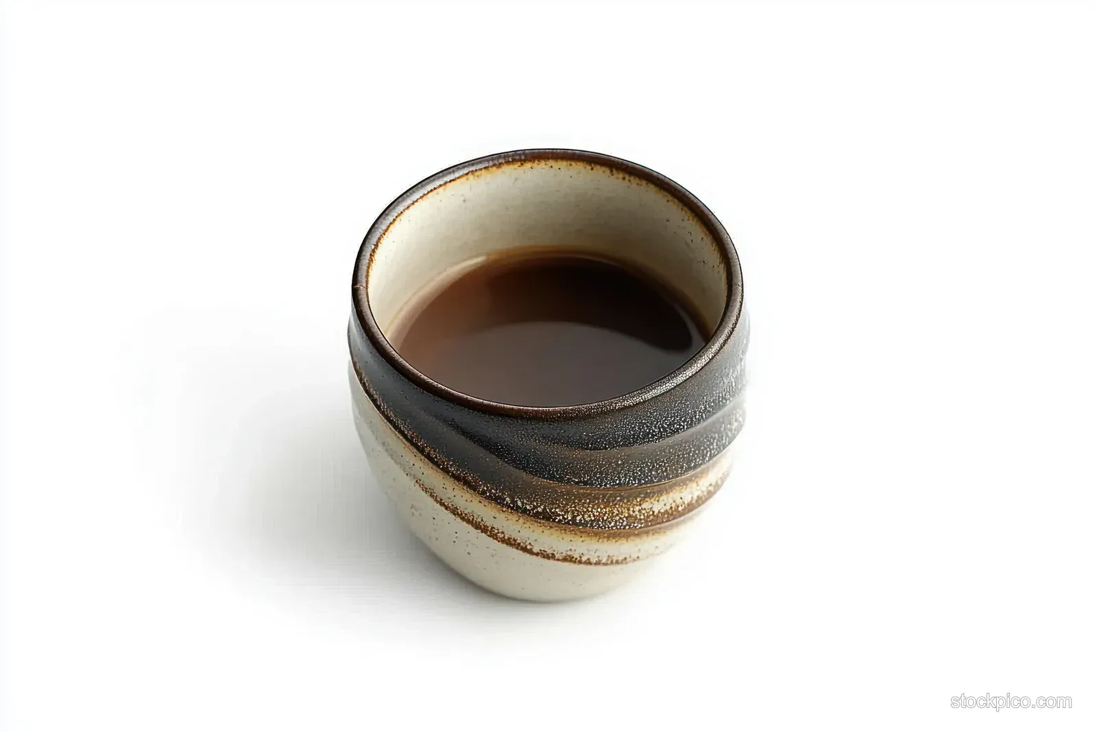 A ceramic coffee mug filled with dark espresso sits on a white background, showing a swirled brown and beige glaze.