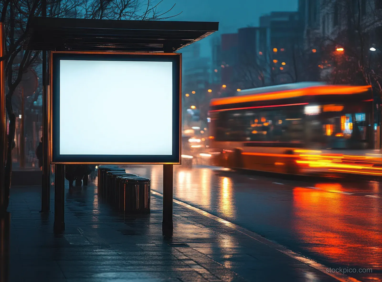 An empty illuminated bus stop billboard glows on a rain-wet street as an orange bus streaks by with motion blur.