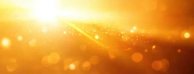 Radiant sunburst glowing through warm abstract haze background with golden light rays