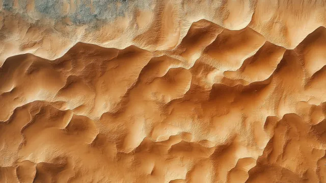 Aerial view of orange desert sand dunes with layered ridges and long shadows