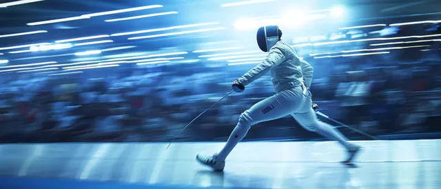 A male fencer lunges forward on the piste under bright arena lights.