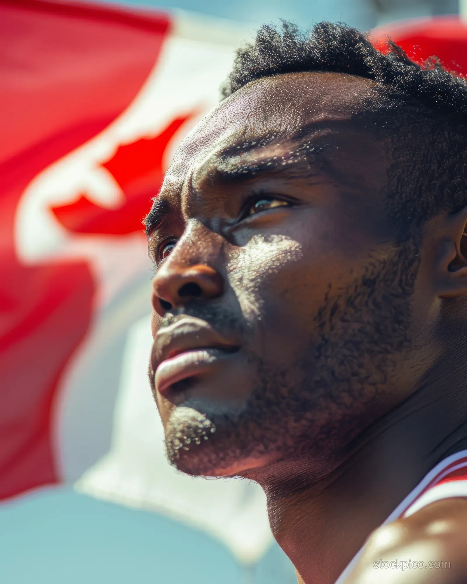 Decathlete at the track starting line with a Canadian flag waving behind, showing race-day intensity.