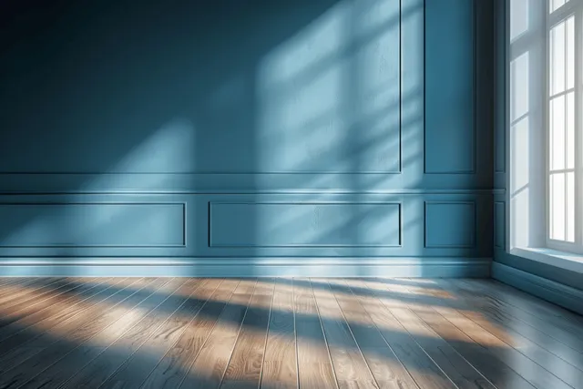 Sunlit blue wall and wooden floor with striped window shadows in a minimal interior corner.