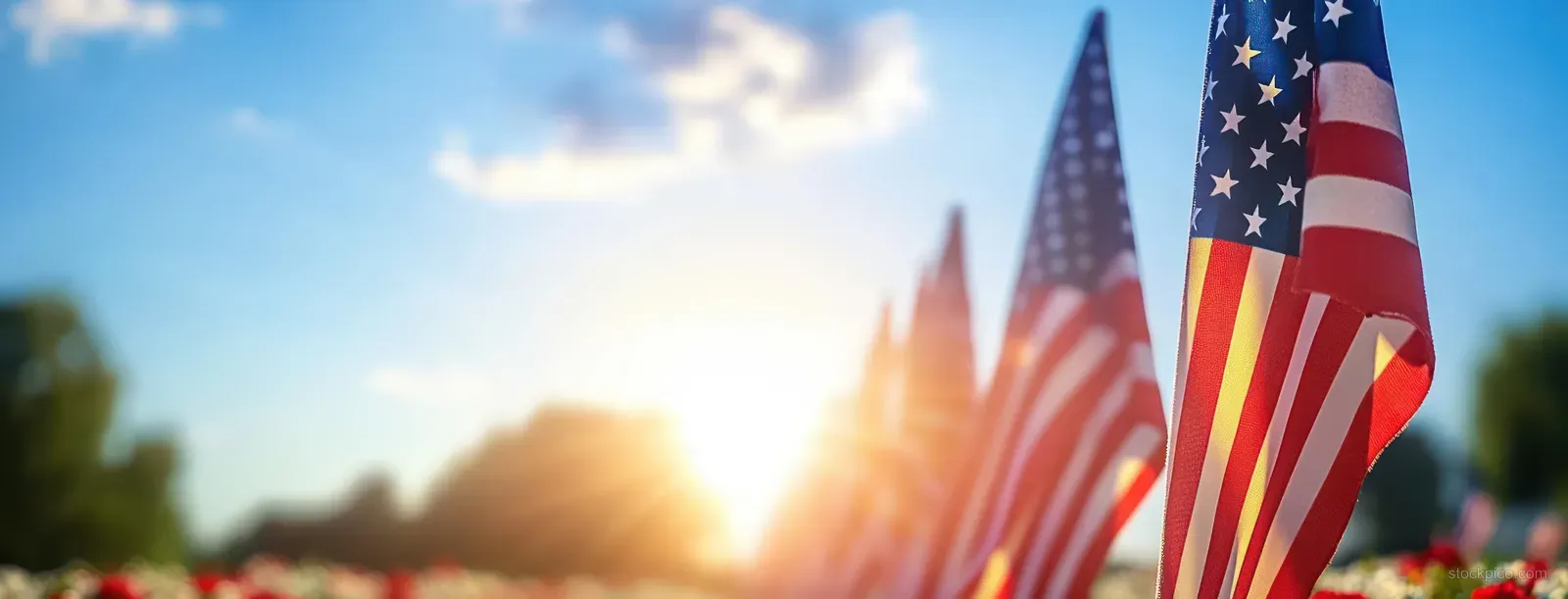 American flags waving outdoors at sunrise with sunbeams and softly blurred background crowd.