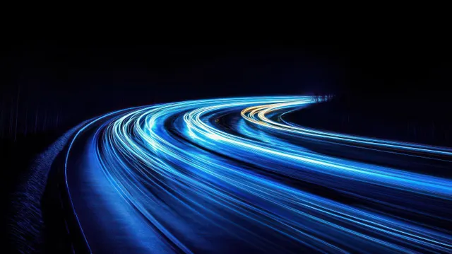 Blue and white light trails curve along a dark highway at night.