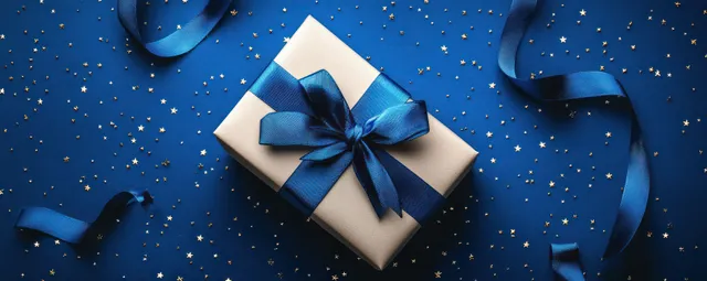 Dark blue gift box with ribbon and star confetti flat lay on festive blue backdrop