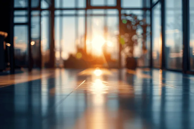 Sunlit modern office hallway with panoramic windows, blurred desk silhouettes, bright flares