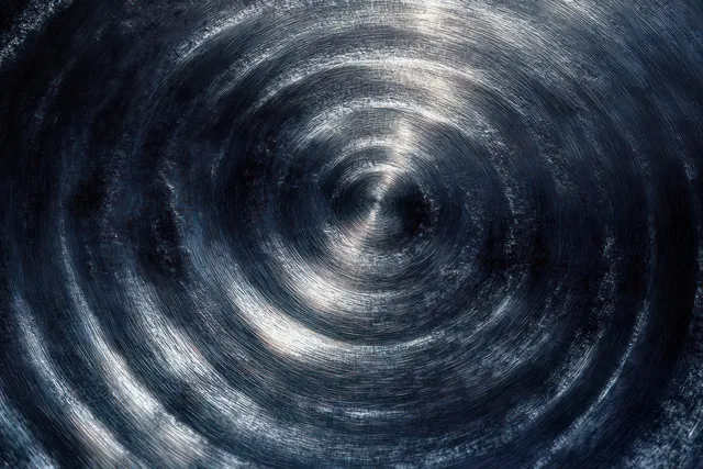 Close-up of brushed steel with concentric circular swirls and reflective highlights on a textured surface.