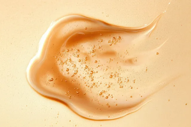 Golden viscous liquid ribbon with suspended air bubbles spread across a smooth glossy surface.