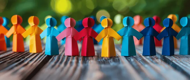 Colorful paper cut-out figures hold hands in a human chain on a wooden surface