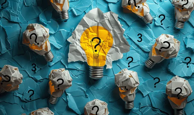 Glowing yellow lightbulb surrounded by crumpled lightbulb icons and question marks on torn blue paper.