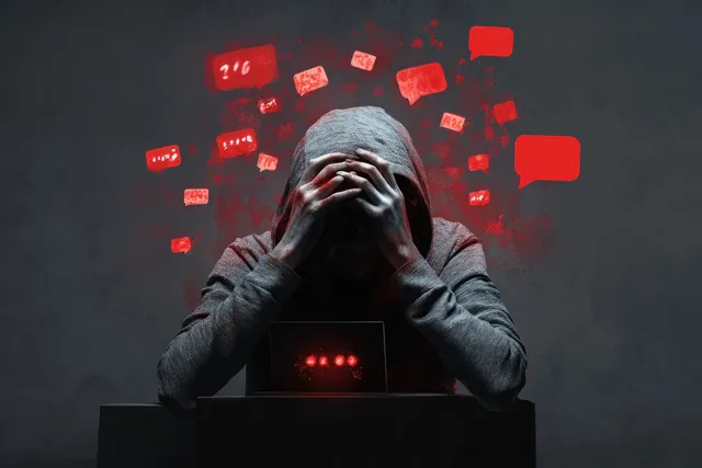 Hooded teen covers face at laptop as red hateful messages float around