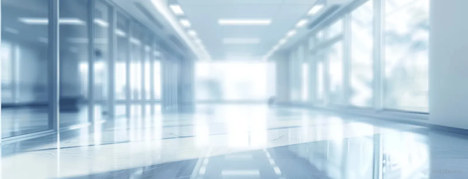 Blurred light blue office corridor with panoramic windows, reflective floor, and soft ceiling lighting.