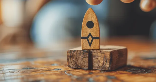 Wooden rocket launch icon standing on rustic desk with blurred office background