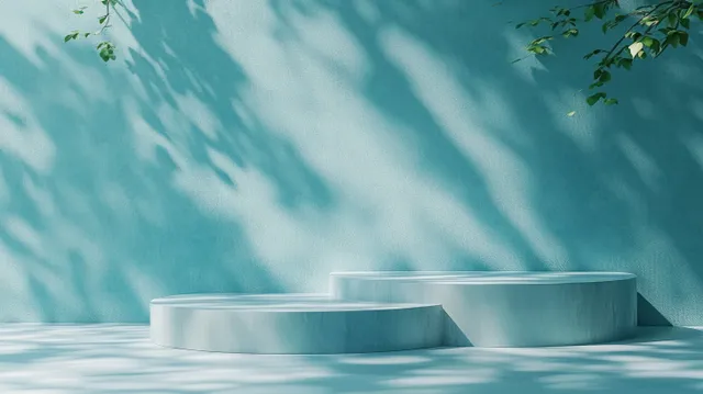 Two-tier round concrete platforms against a textured teal wall with soft dappled leaf shadows.
