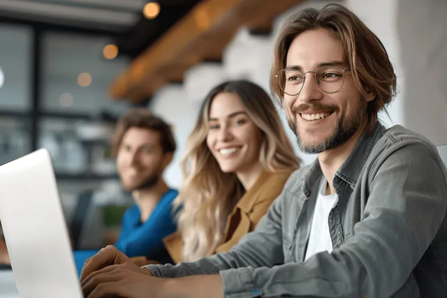 Smiling project manager and colleague collaborate on laptop at office desk with bokeh