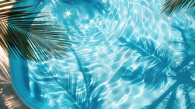 Top view of turquoise pool water with palm leaf shadows and sparkling ripple patterns under sunlight.